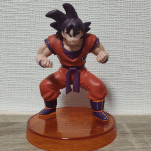 Action figure of a muscular martial artist in an orange gi with a purple belt, fists raised, on a round orange base. (Dragon Ball style)