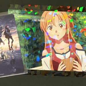 Anime scene with a surprised girl on a bench, confetti overlay, and a Sword Art Online Blu-ray case nearby.