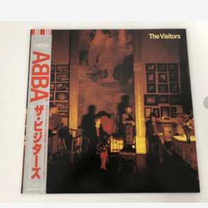 ABBA – The Visitors vinyl album cover showing a dimly lit room with seated figures and framed photos on the wall.
