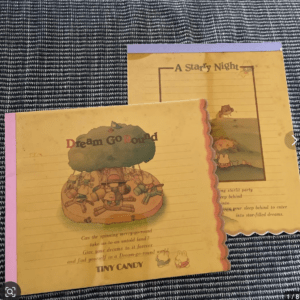 Two yellow children's booklets on a dark textured surface; front cover shows a carousel scene and the title 'Dream Go Round' with colorful illustrations.