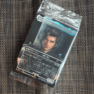 Packaged Japanese trading card featuring a portrait of a man with dark, spiky hair, sealed in clear plastic on a dark woven surface.
