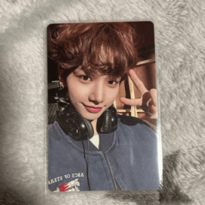 Portrait-style photo card of a young person with brown hair wearing headphones around the neck, flashing a peace sign to the camera.