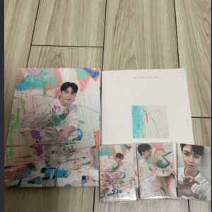Collection of color-splashed photo books and cards featuring a young man in white, arranged on a wood floor.