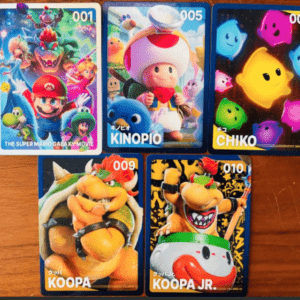 Five collectible cards laid on a wooden surface; visible titles include 001 The Super Mario Galaxy Movie, 005 Kinopio (Toad), 007 CHIKO, 009 KOOPA, and 010 KOOPA JR.