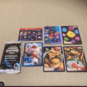 Six Nintendo character cards laid on a tatami mat, including Mario, Toad, Koopa, Koopa Jr., and colorful creatures; a sealed card pack is on the left.