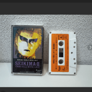 Cassette tape with an orange label sits next to a jewel case cover featuring a stylized yellow-and-black portrait and the text 'SEIKIMA-II FROM HELL WITH LOVE'.