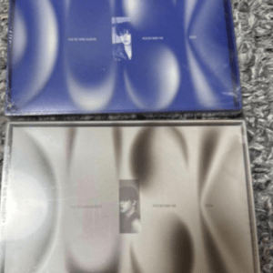 Two CD cases on a carpet: blue case with abstract circles and a small central photo, and a silver case with a matching abstract design.