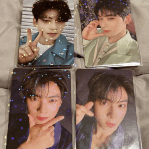 Set of four glossy photo cards of a young male K-pop idol posing in different ways with star confetti overlay, laid on a gray surface.