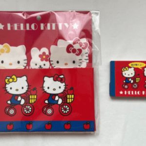 Hello Kitty red fabric set featuring two characters riding bicycles, with an apples border and blue trim, packaged in plastic.