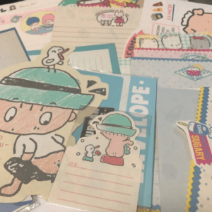 Colorful collage of kawaii stationery: cartoon characters, envelopes, stickers, and decorative papers scattered across a desk.