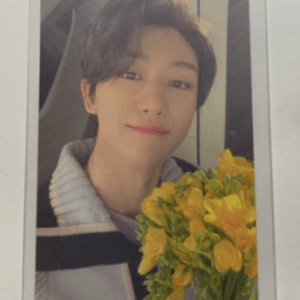 Young man smiling while holding a bouquet of yellow flowers indoors, wearing a light sweater.