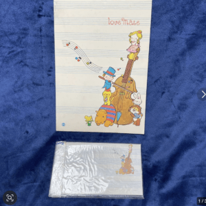 Children's music-themed notebook with a colorful illustration of people and animals around a large violin and musical staff; text 'Love Nate' appears at top.