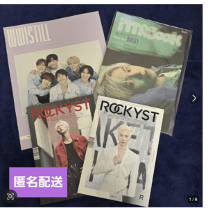 Several K-pop magazines spread on a dark blue surface, including two ROCKYST issues and a lavender cover with a group photo.