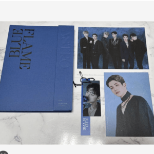 Blue album box set with a group photo and portrait cards for a K-pop boy band, resting on a marble surface.
