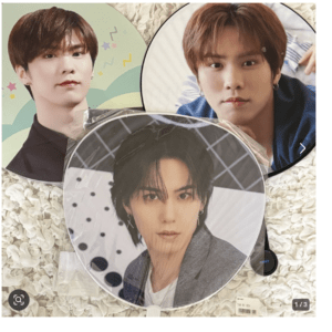 Three round handheld fans featuring close-up photos of male idols, laid on a cream textured surface.