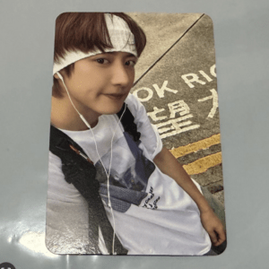 Teenager taking a selfie outdoors, wearing a white headband and white earphones, with a backpack strap visible.