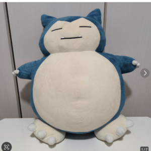 Blue and cream Snorlax plush toy sitting upright with arms spread on a white surface.