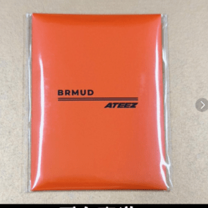 Orange plastic pouch with black BRMUD and ATEEZ branding, sealed in clear plastic wrapper.