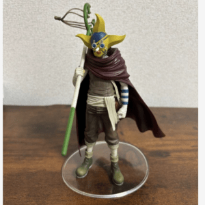 Action figure of a masked adventurer with a yellow star-shaped head, brown cape, and a green-and-white staff on a clear base.
