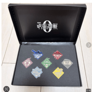 Open black presentation box with a foam insert displaying eight colorful enamel pins, each with unique symbols or characters and a white logo on the inside lid.