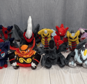 Line of colorful plush toy characters lined up on a light wooden floor, with a Pikachu plush on the far right and various dragon-like figures in the middle.
