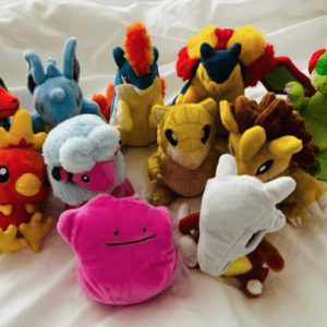 A cluster of colorful stuffed animals arranged on a white surface, featuring pink, yellow, blue, and green plush toys in various shapes.