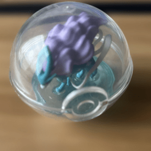 Clear glass ball ornament containing purple and teal hair ties and a silver clip, resting on a wooden surface.