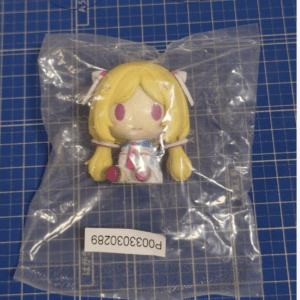 Small anime-style chibi figure with yellow hair in a clear bag on a blue grid cutting mat.