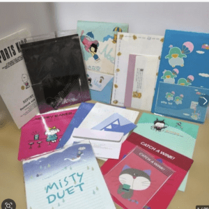 Assorted colorful notebooks, cards, and envelopes with cartoon characters spread on a table.