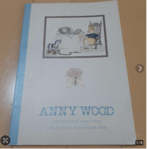 Cover of a children's book titled 'Anny Wood' showing a rabbit at a tea table with a wooden hobby horse nearby ( illustration inside a frame ).