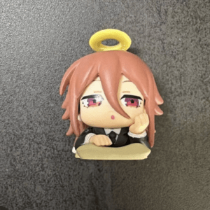 Chibi anime figurine with pink hair and pink eyes, resting its head on a hand with a yellow halo above the head.
