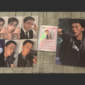 Set of glossy photo cards featuring a male singer in different poses, arranged on a woven surface, with a pink collectible card in the middle.