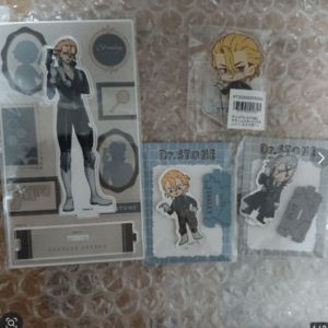 Chibi Dr. Stone character stickers and key visuals on bubble wrap, including blond-haired character in black outfit and various packaging designs.