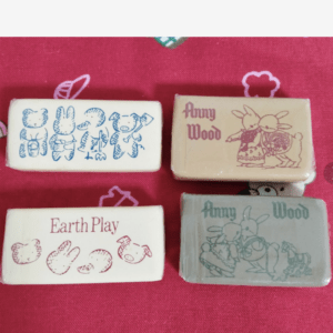 Set of four small animal-themed erasers on red fabric; prints include 'Earth Play' and 'Anny Wood' with cartoon animals.