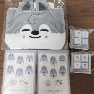Cute Wolf Chan-themed product set: gray and white plush bag with ears, plus sticker sheets and small eraser cubes in plastic packaging on a wooden table.