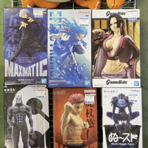 Orange dragon/dragon-like plush toy lounging on a metal display rack with boxed anime figures arranged below, including Grandista and Maximatic figures featuring characters in dynamic poses.