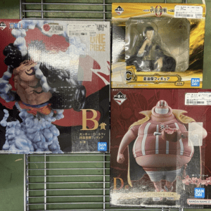 Three boxed anime figures on a metal shelf, including One Piece merchandise with price stickers and Banpresto/ Namco logos visible.