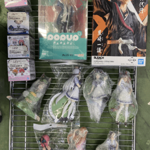 Display rack of packaged anime figures and statues, including a POP UP PARADE figure in the center and a Bleach box on the right.