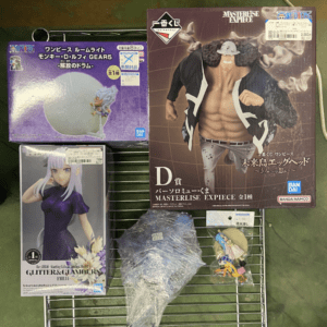 A metal rack holding several boxed anime figures: a large Masterpiece One Piece box with a shirtless figure on the right and purple boxed figures on the left.