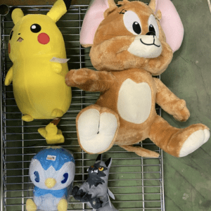 Four stuffed animals on a metal rack: a large yellow Pikachu-like plush, a brown bunny, a blue penguin, and a small gray wolf.