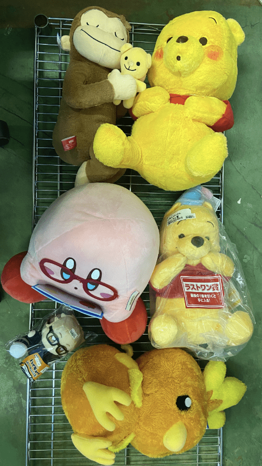 Captura De Pantalla 2026-07-02 a Las 184605 - Articulos Japan (post Box Japan) Assorted stuffed toys on a metal rack: a yellow Winnie-the-Pooh bear, a brown monkey, a pink round character with glasses, and a small yellow bear in plastic. Articulos Japan (Post Box Japan)