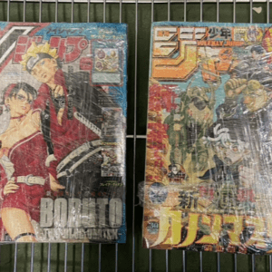 Two wrapped manga volumes on a metal rack; left shows Boruto with Naruto characters in red outfits, right shows a Jump issue with multiple heroes in colorful cover art.