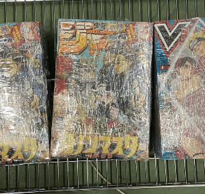 Three wrapped Japanese action-figure boxes on a metal rack, with colorful illustrated covers.