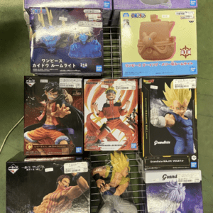 Assorted anime action-figure boxes (One Piece and Dragon Ball) arranged on a metal rack, with purple One Piece boxes on top and various Grandista boxes on the lower shelves.