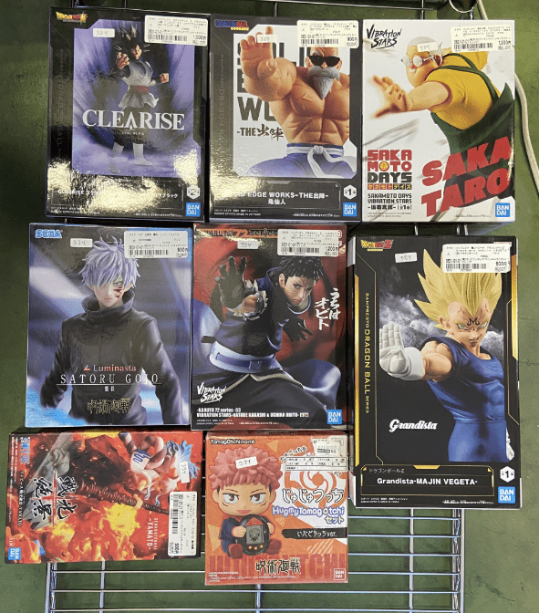 Captura De Pantalla 2026-07-05 a Las 090912 - Articulos Japan (post Box Japan) Boxed anime figures on a metal display rack, featuring characters like Satoru Gojo and Dragon Ball Z figures in their packaging. Articulos Japan (Post Box Japan)