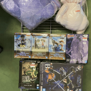 Two large plush toys on a metal rack: a purple Gengar with red eyes and a white creature with blue eyes, both in plastic wrap.