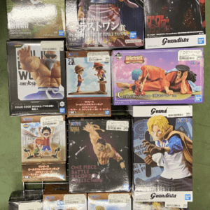 Shelf with stacked anime figure boxes (One Piece, Dragon Ball, Grandista) on a green floor display.