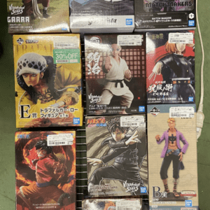 Stacked boxed anime figures on a metal display rack, featuring characters from One Piece and Naruto among others in a store setting.