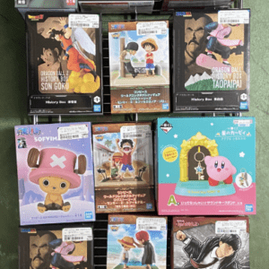 Row of anime figure boxes on a metal rack, featuring Dragon Ball and One Piece characters in colorful packaging on a store floor.