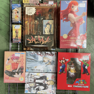 Boxed anime figure collection displayed on a black metal rack, including a tall red-haired character box on the right and multiple colorful figures in front and center.